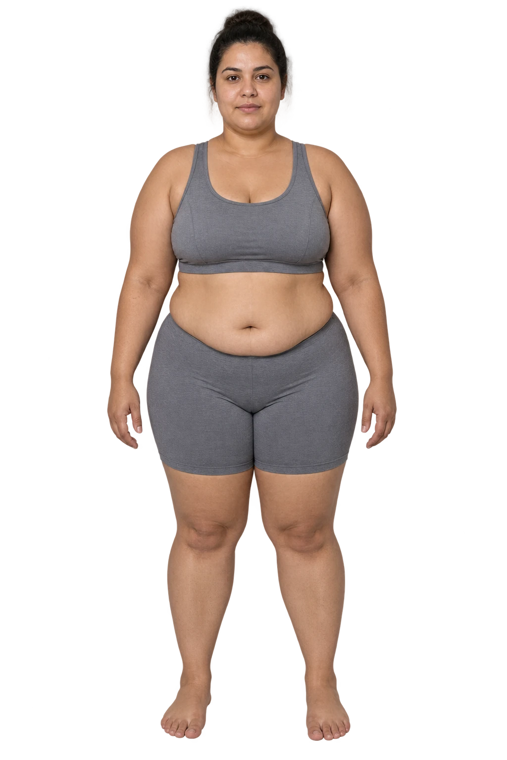 Mulher de frente, com cabelo escuro em coque, top e short cinza e pés descalços.